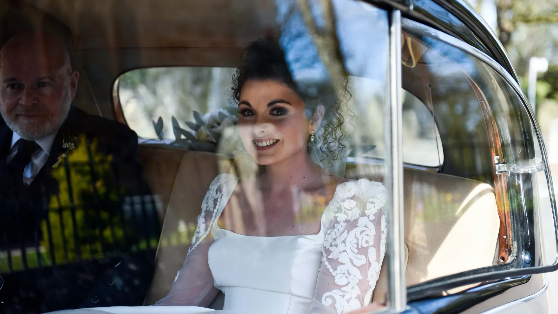 Bride and Father travelling in the back of the Classic Rolls-Royce. Bride looking at the photographer through the window.